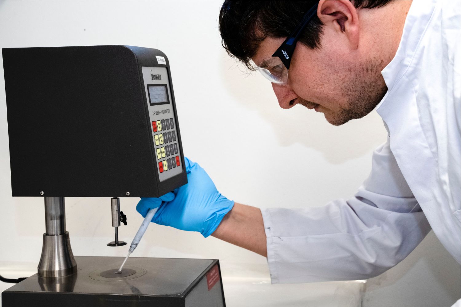 Un hombre con bata blanca vierte algo de una pipeta sobre una superficie